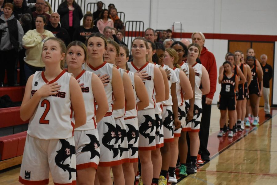 Girls varsity basketball captured showing their respect during the National Anthem. 