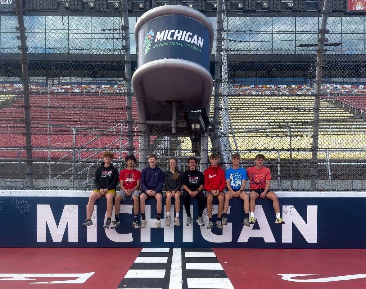 The boys cross country team along with individual qualifier Abby Dice pose for a photo at Michigan International Speedway for the state competition.