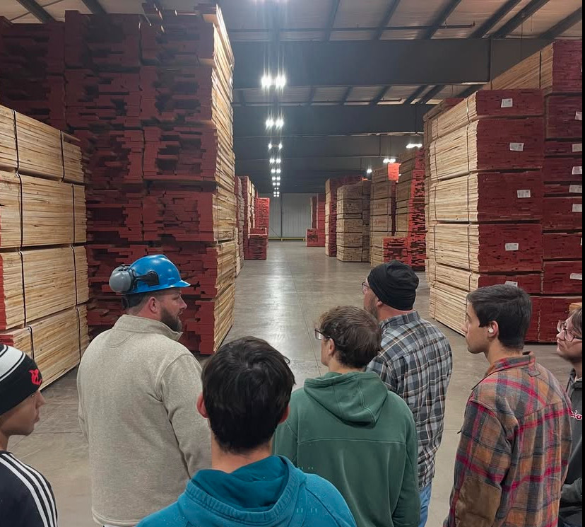 A group of woodshop students listen intently as they take a tour through the shop.