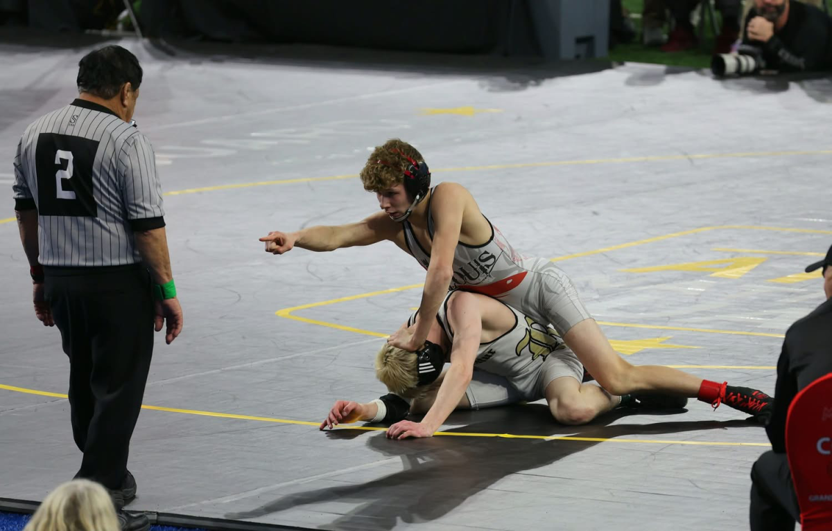 113 pound state champion Owen Fogel points at a camera as he takes down his opponent..